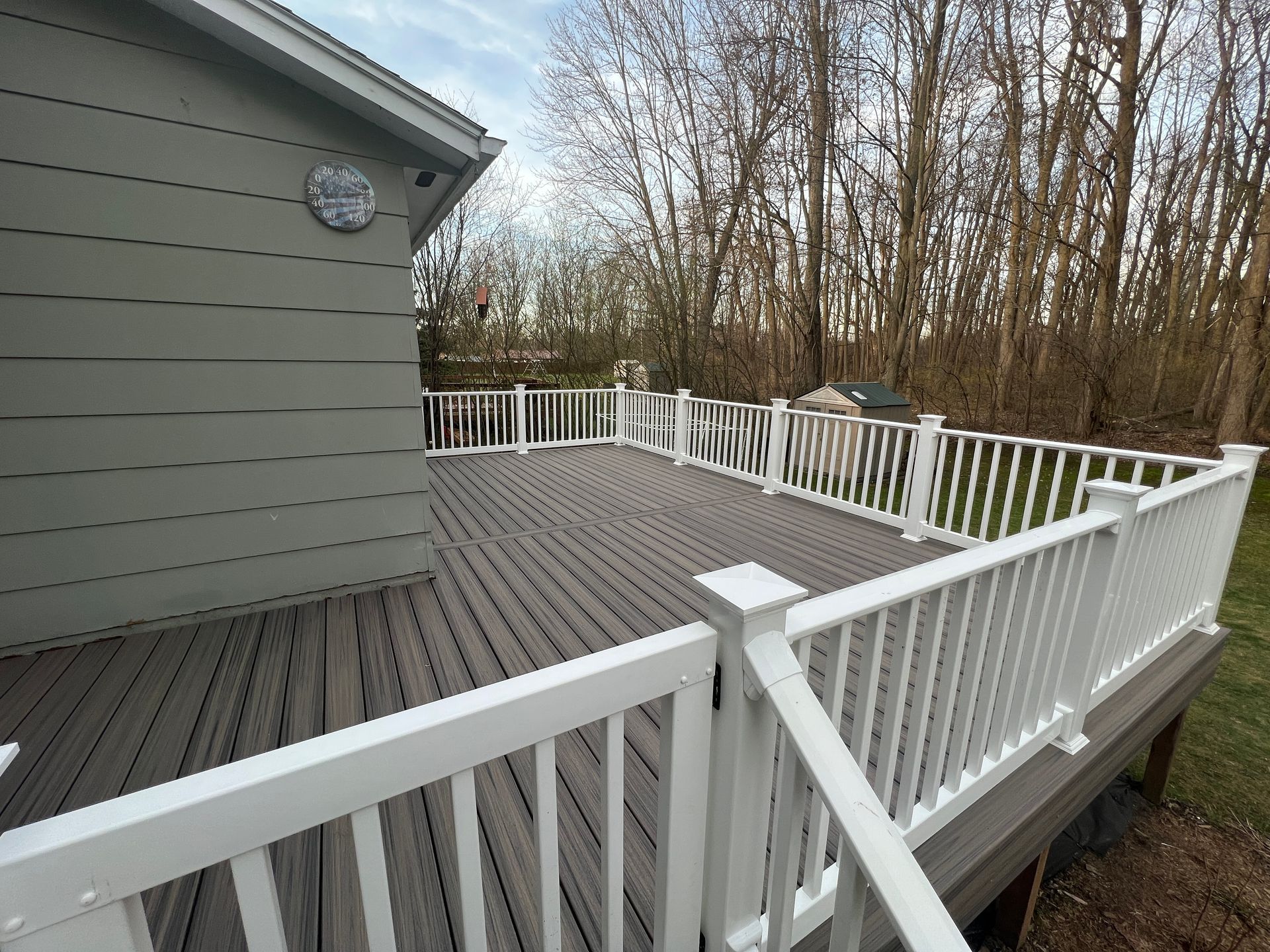 A large deck with a white railing and trees in the background