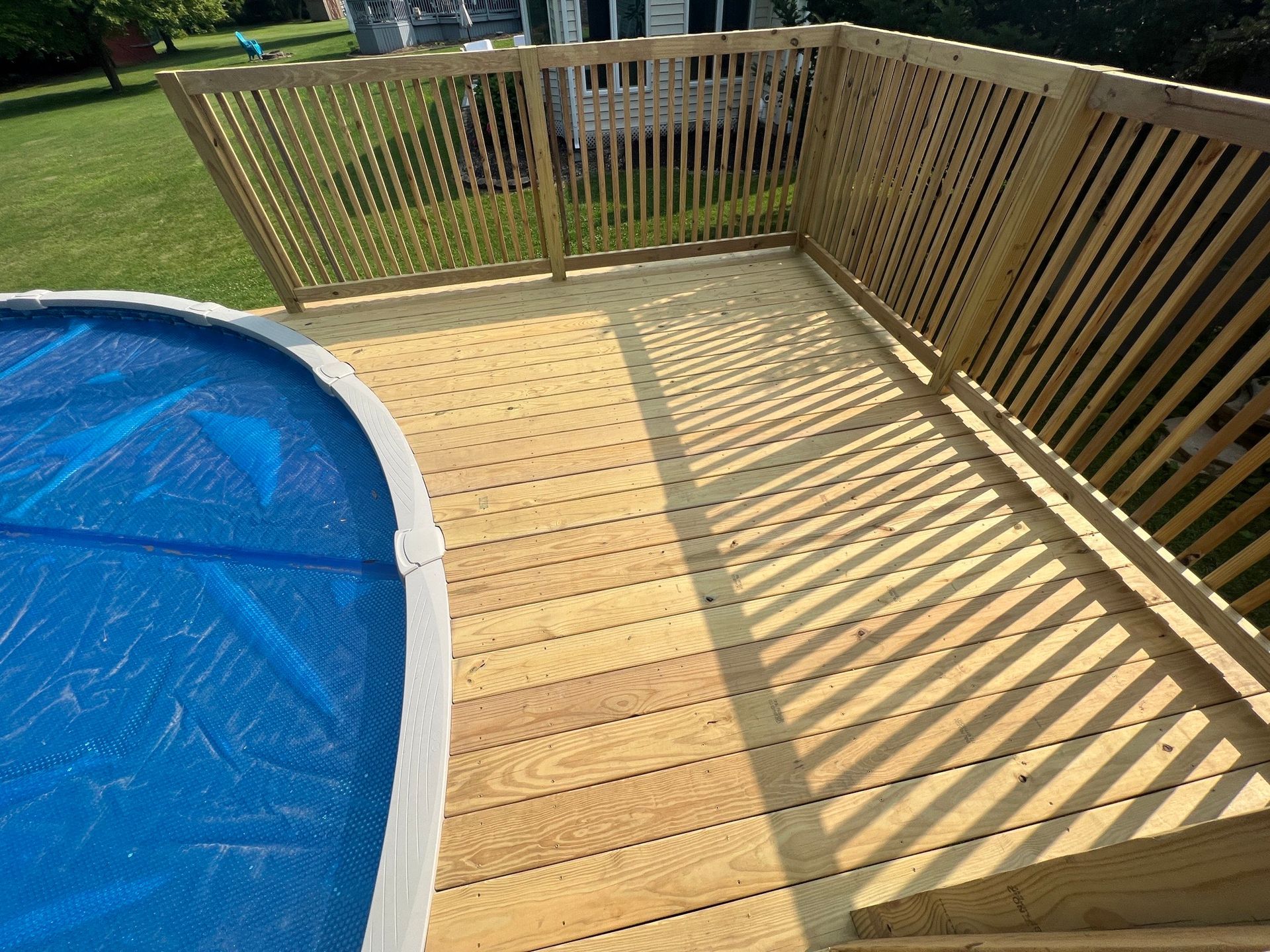 A wooden deck next to a swimming pool with a blue tarp on it.