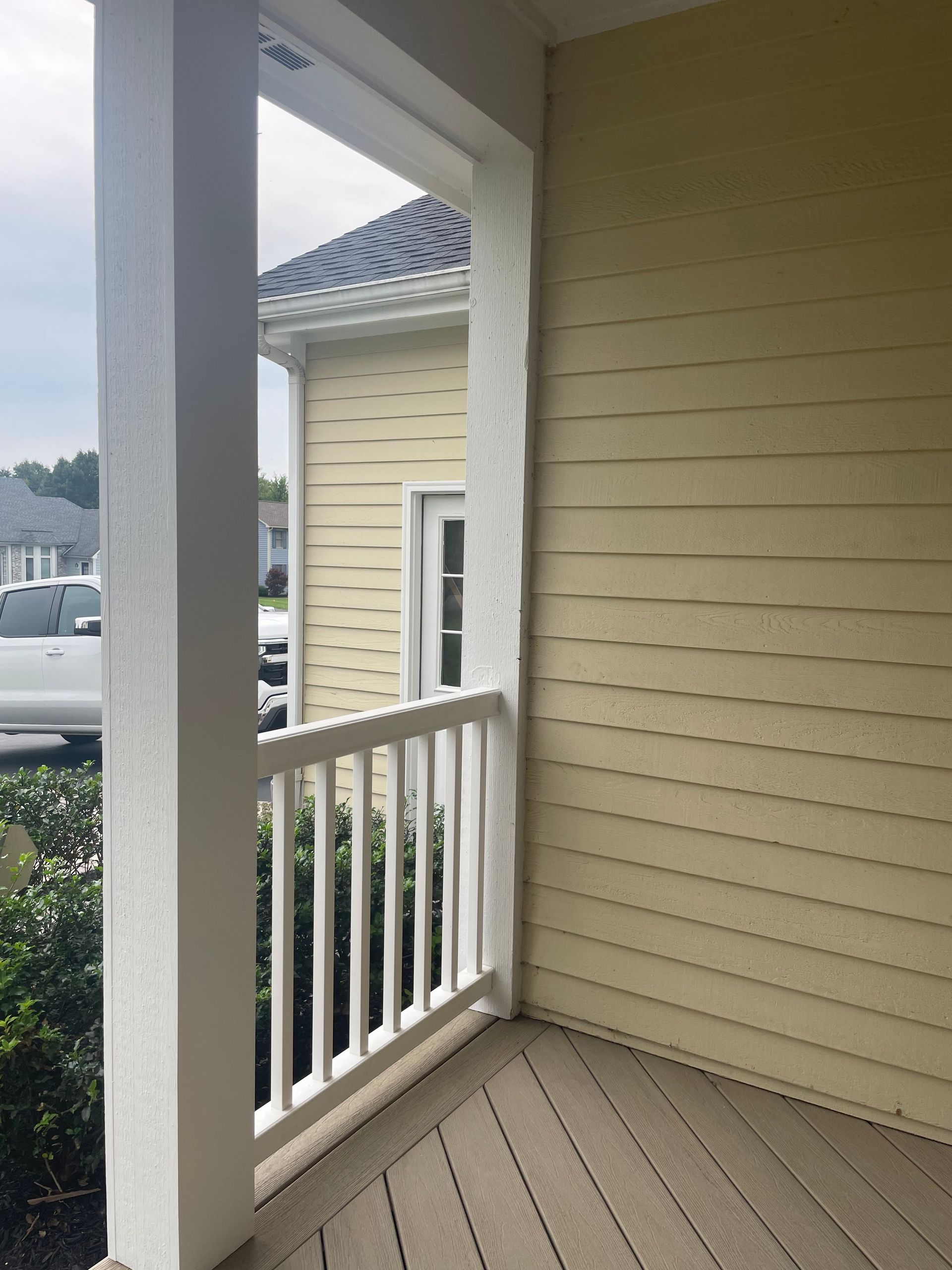 An empty porch with a white railing and a yellow house in the background