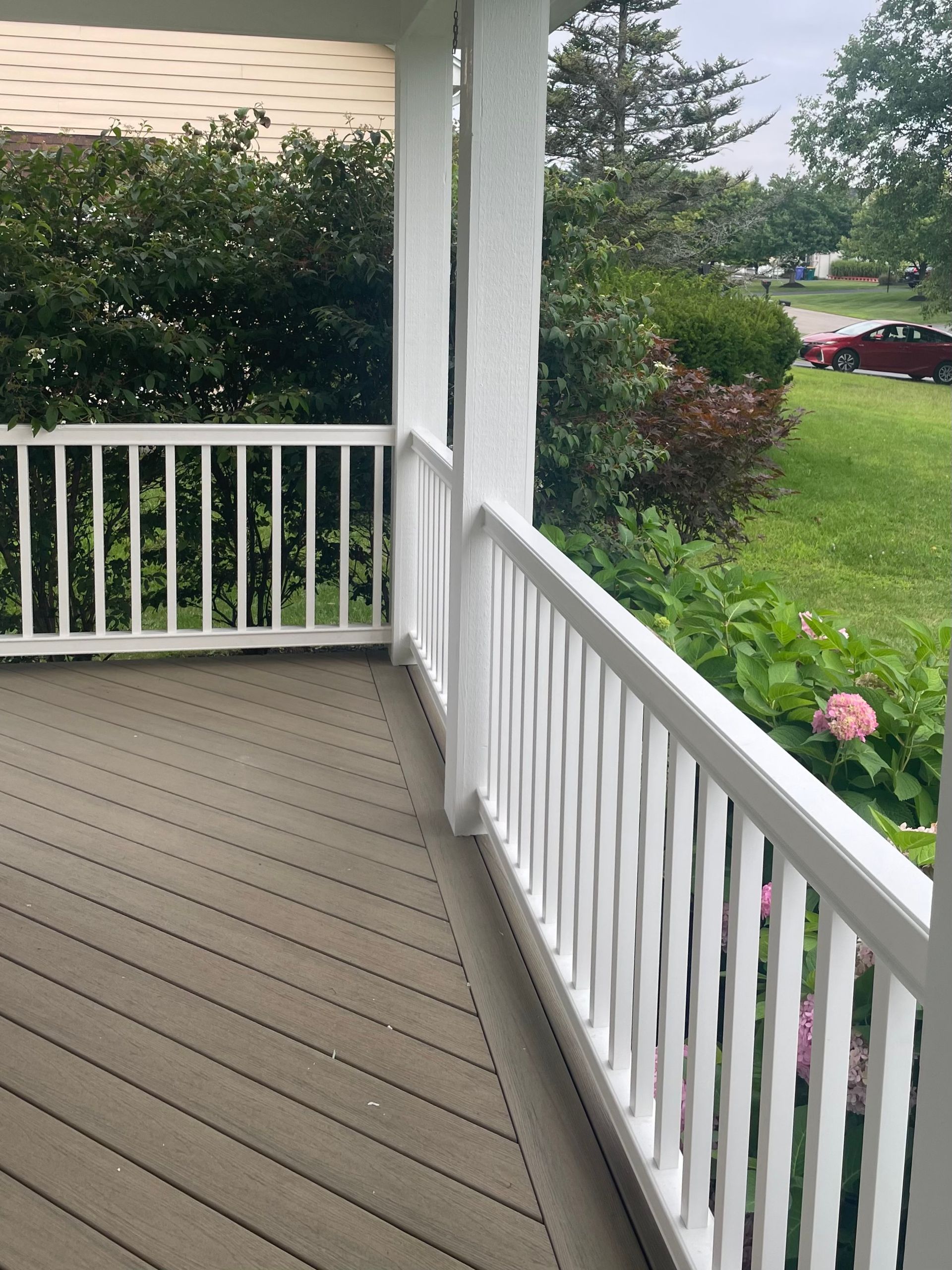 A porch with a white railing and a car parked in the background