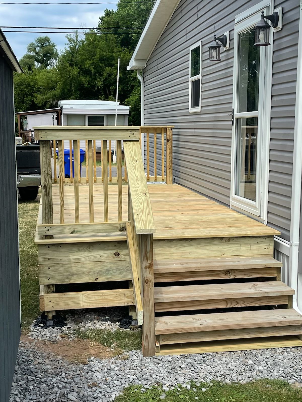 Wooden deck with stairs leading to a gray-sided building. Gravel ground.