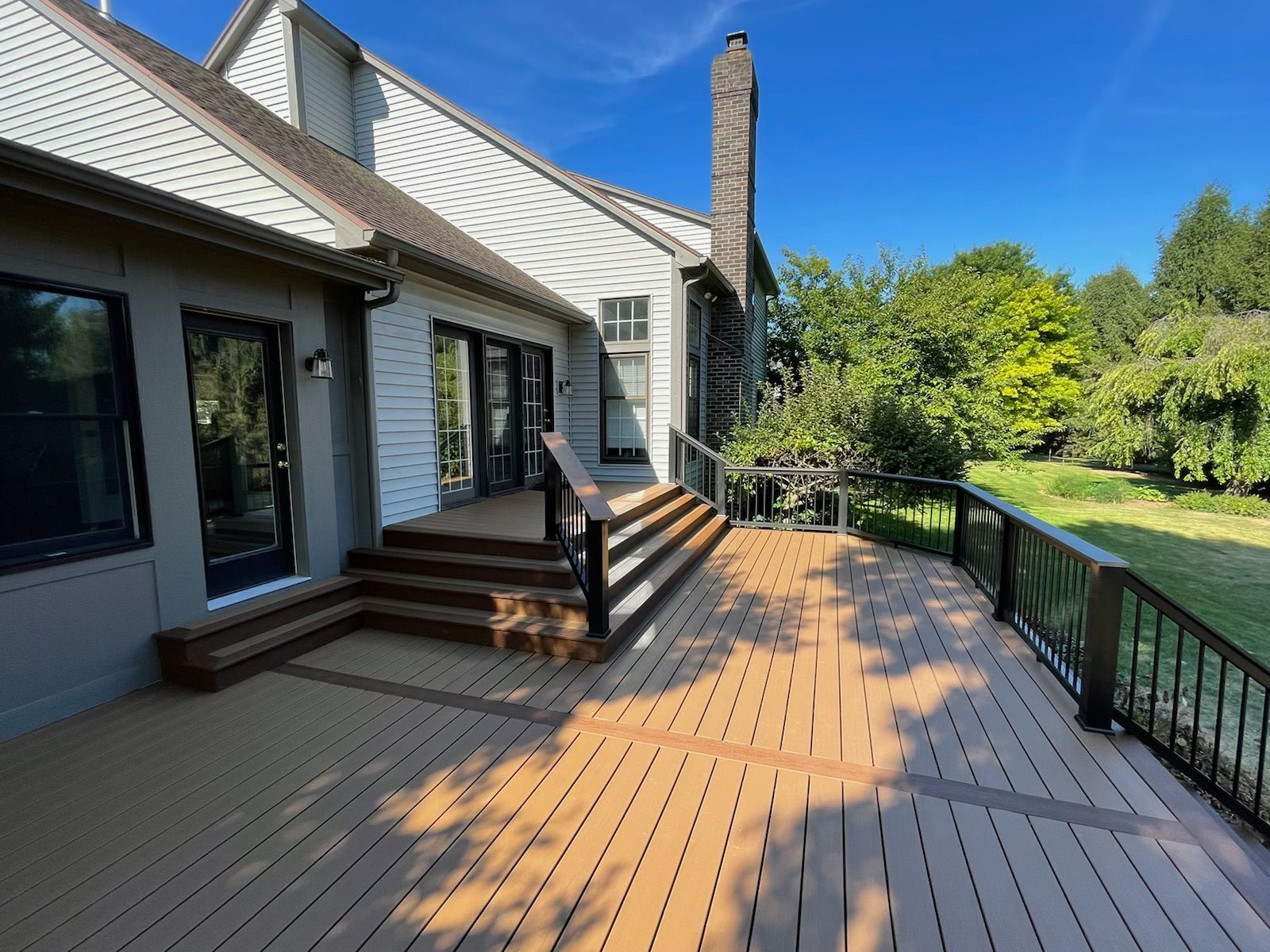 Backyard deck with brown composite decking, black railing, and a house in the background.