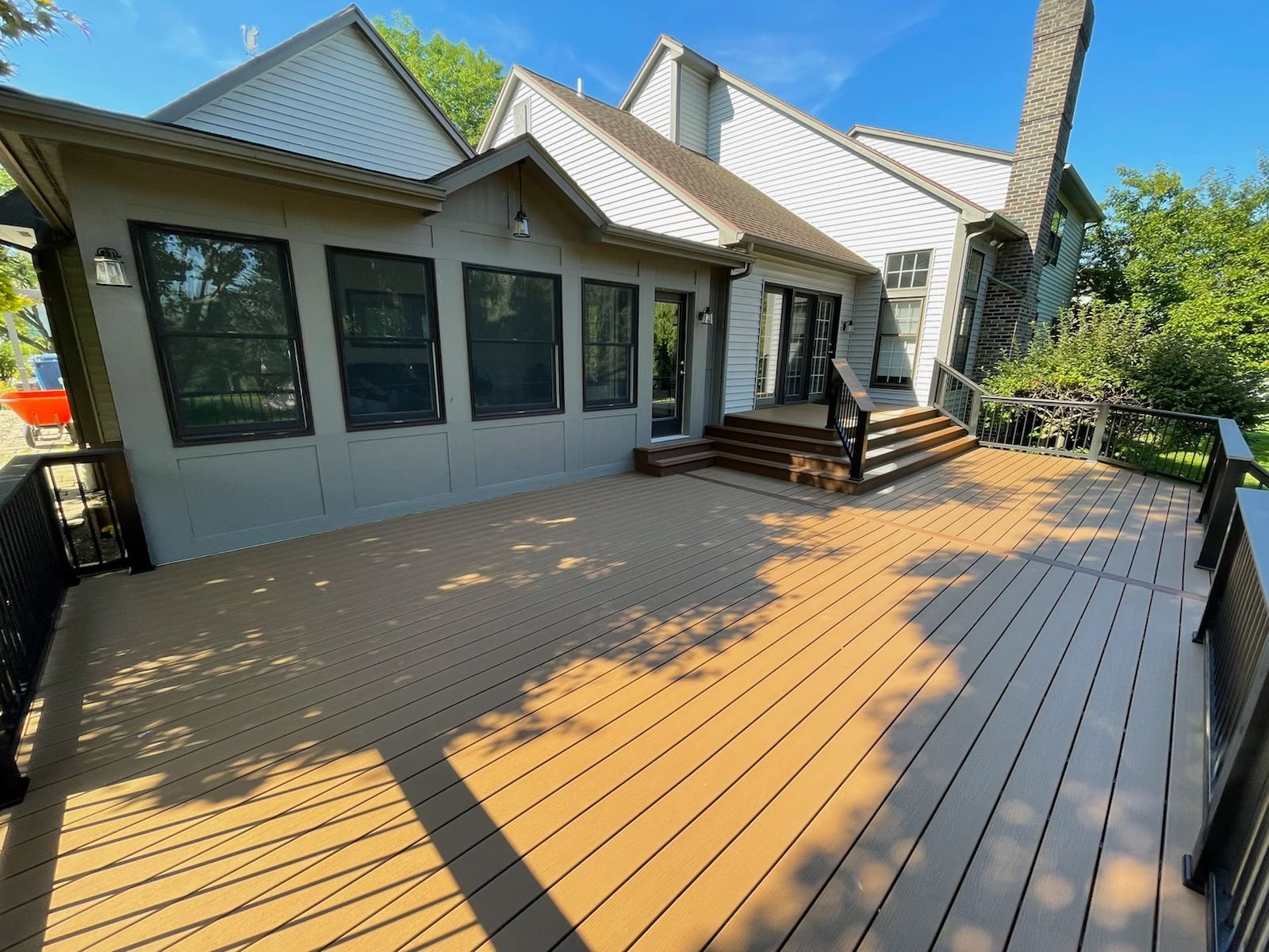 A large wooden deck attached to a house with a light gray exterior. Sunny day.
