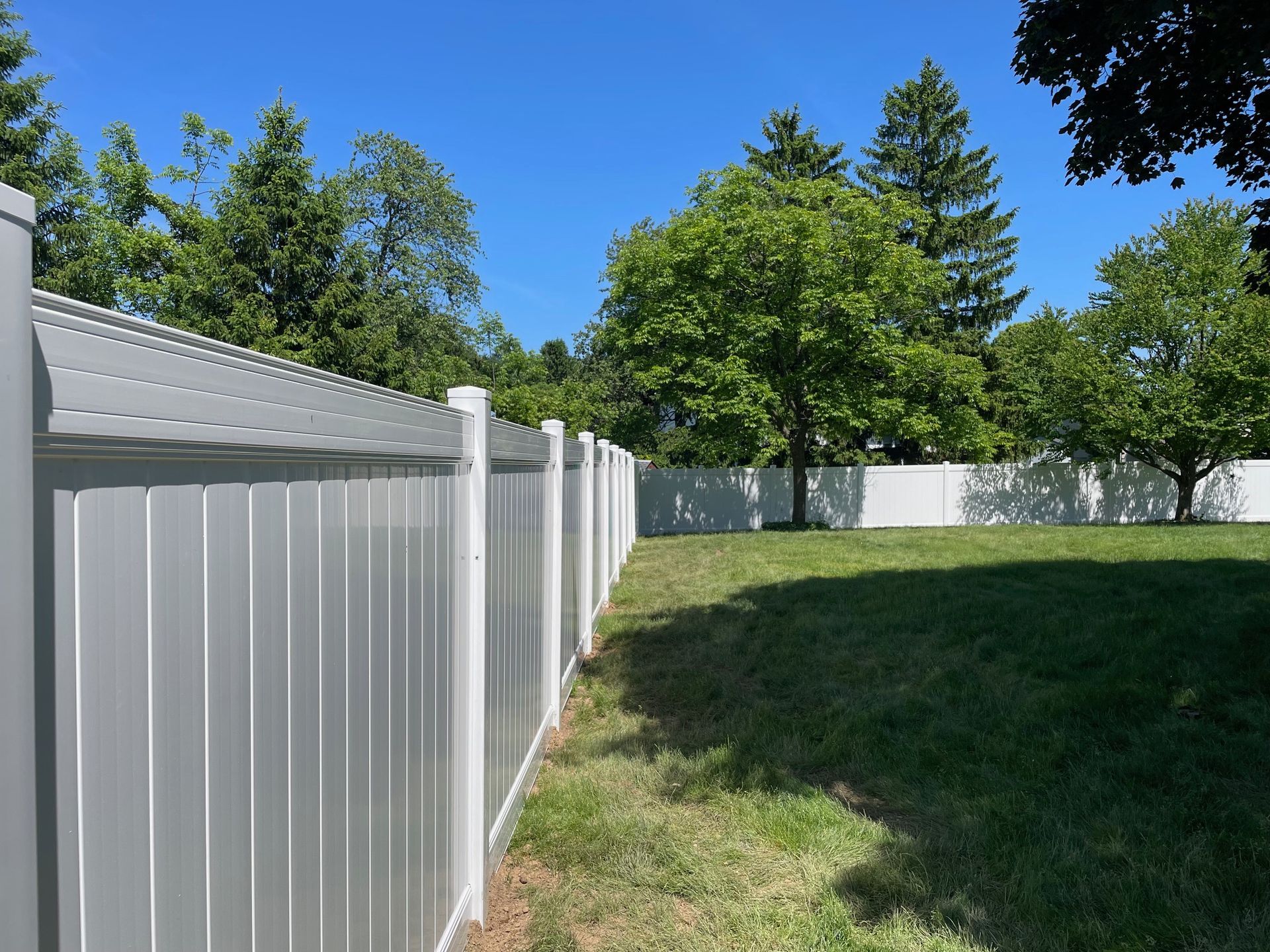 A white fence surrounds a grassy yard with trees in the background