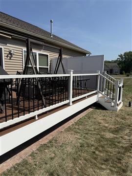 An elevated deck with a white railing and black metal balusters, featuring a black porch swing and a white privacy screen.