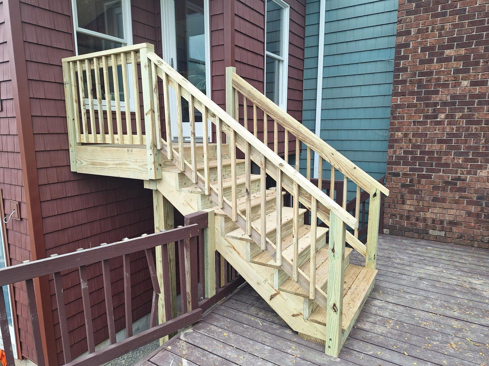 Wooden exterior staircase with railing leading down from a brown building to a deck.