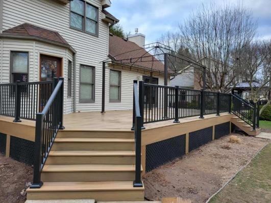 A wooden deck with stairs and a black railing in front of a house.