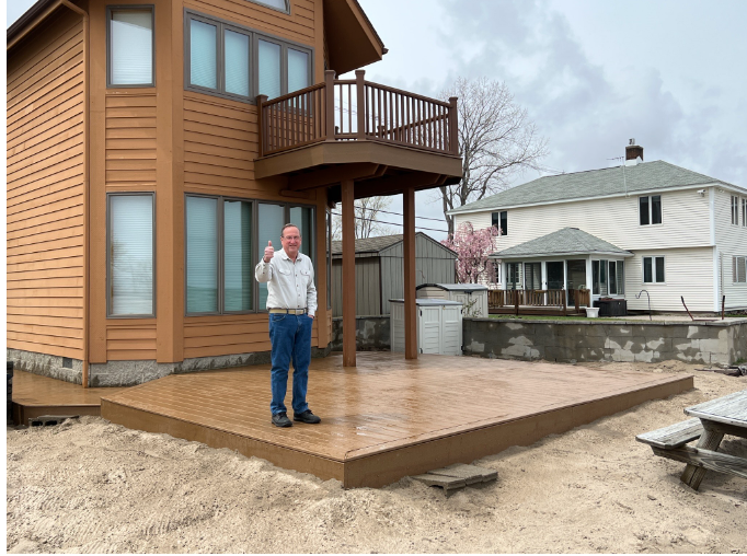 A wooden deck with stairs and a white railing is in front of a house.