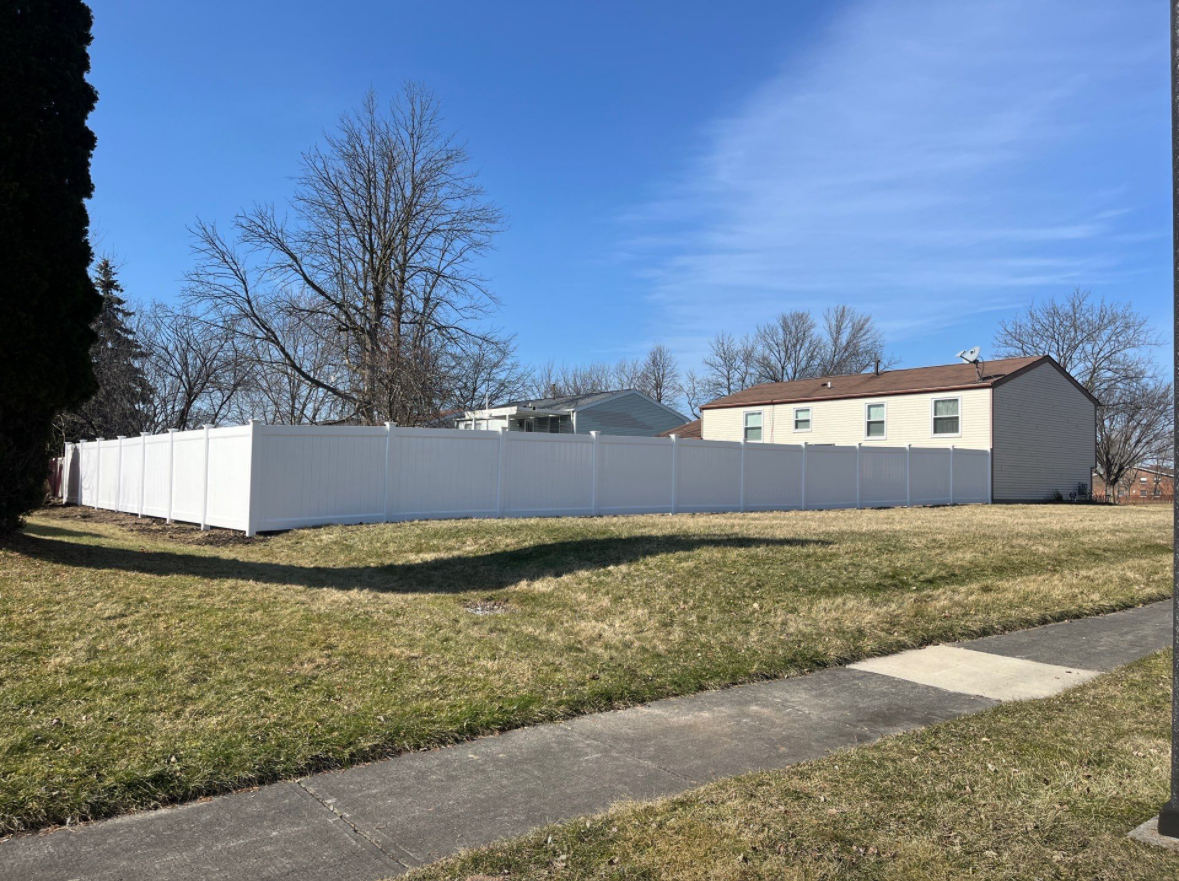 A white fence surrounds a grassy field with a house in the background.