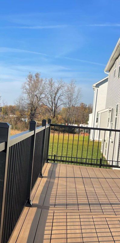 View from a deck overlooking a green lawn and trees under a blue sky.