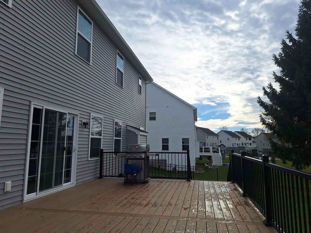 Backyard deck with composite decking, black railing, and grey siding on a house. Cloudy sky.
