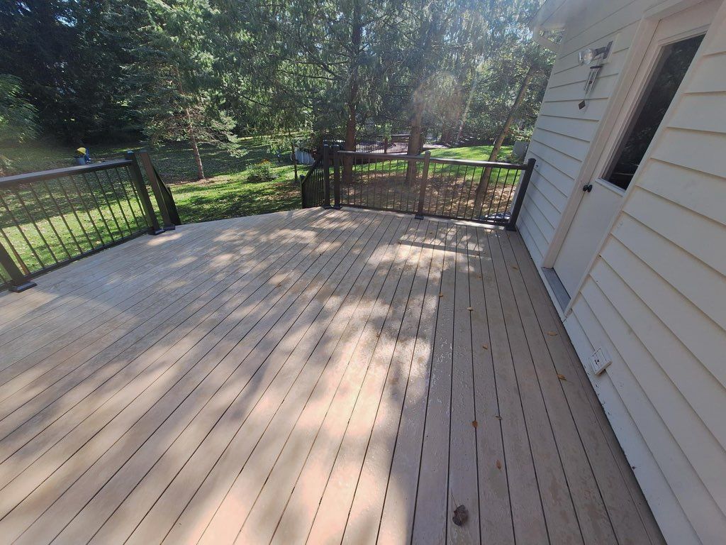 A large wooden deck with a railing and trees in the background.