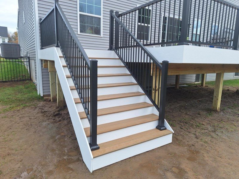 Exterior view of a deck with stairs, black railing, white trim, and brown steps leading to a house.
