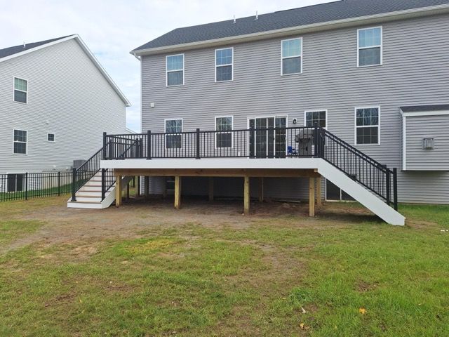 Backyard deck with black railings and white stairs attached to a two-story gray house.