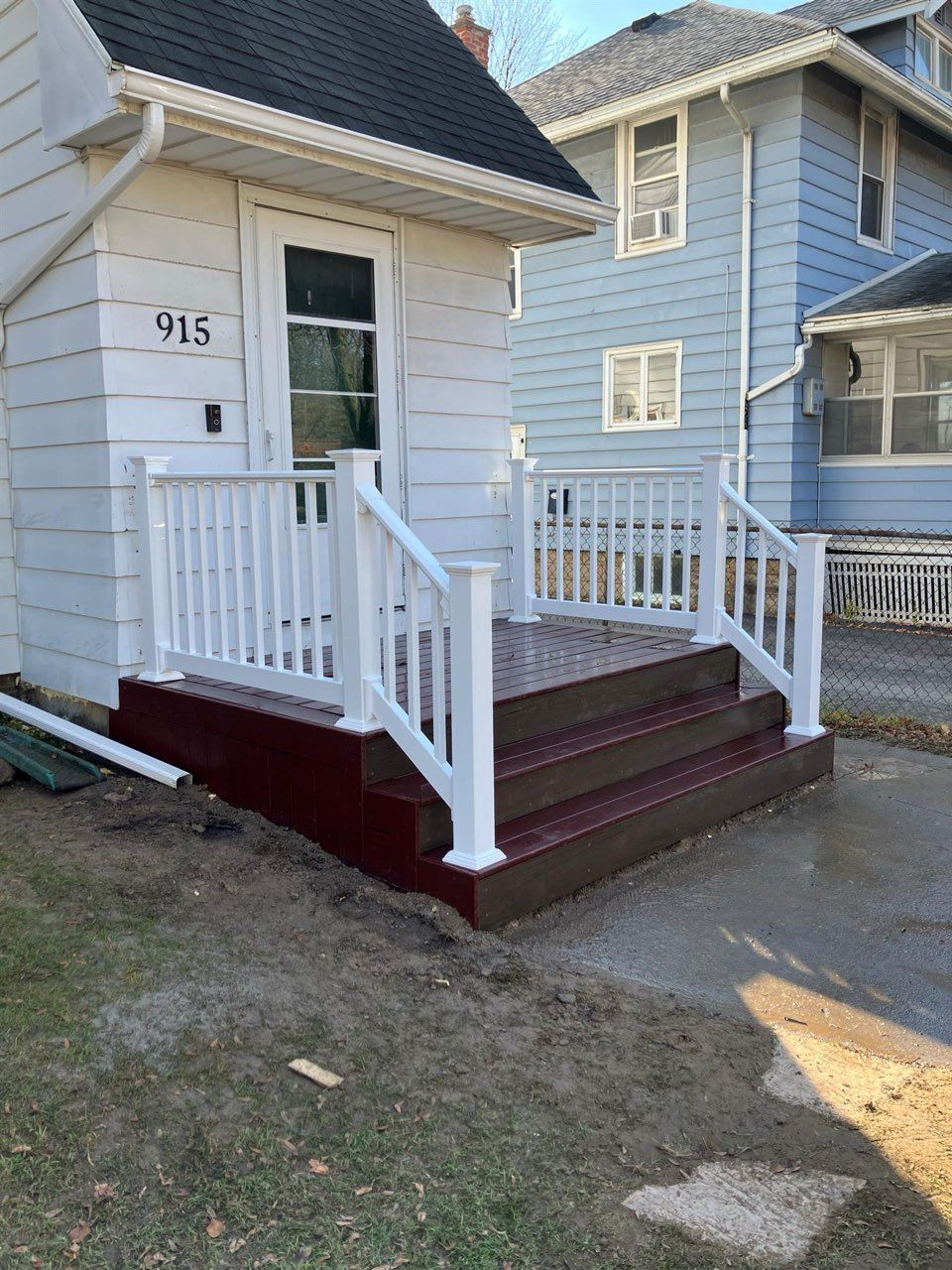 Front porch with white railings, burgundy steps, and a white door labeled 