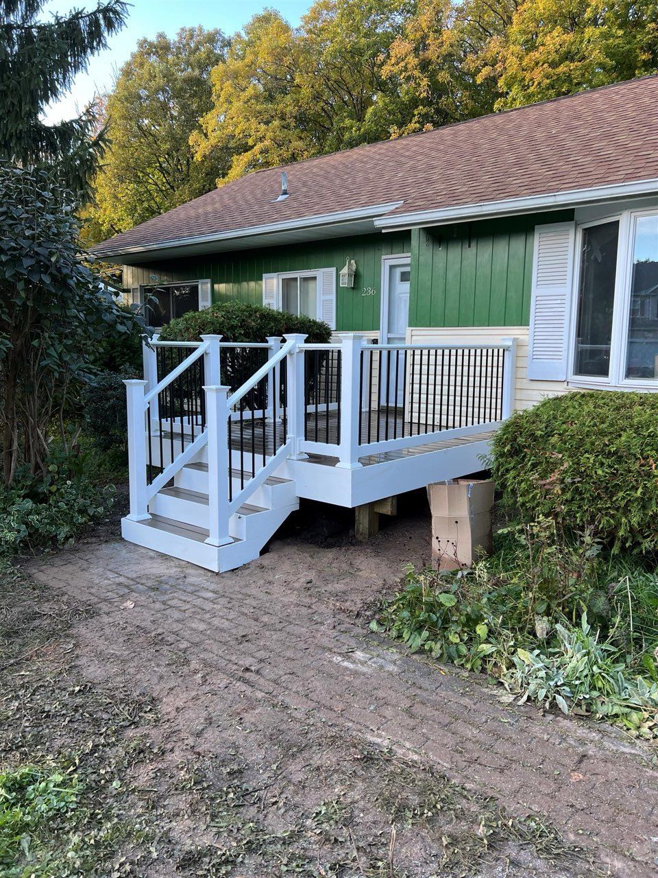 A white deck with black railings and steps in front of a green house with a brown roof.