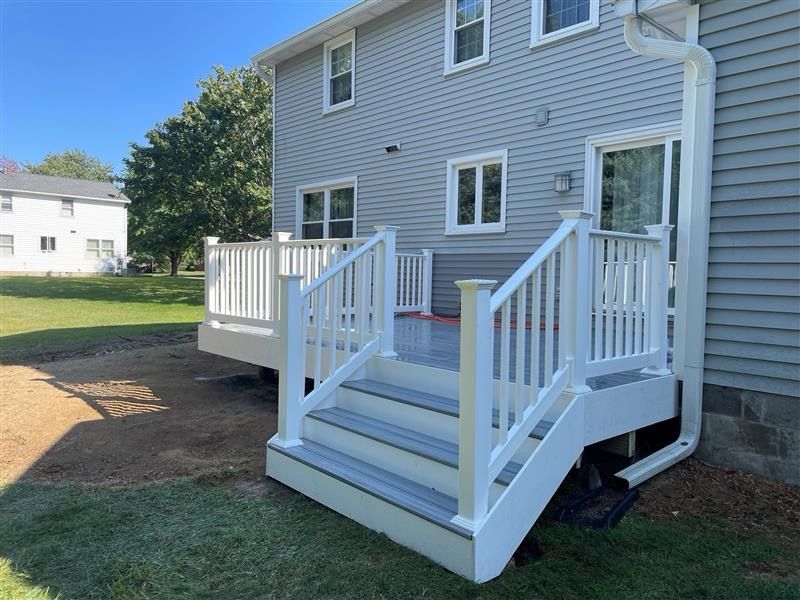 Gray house with white deck and stairs on a grassy lawn.