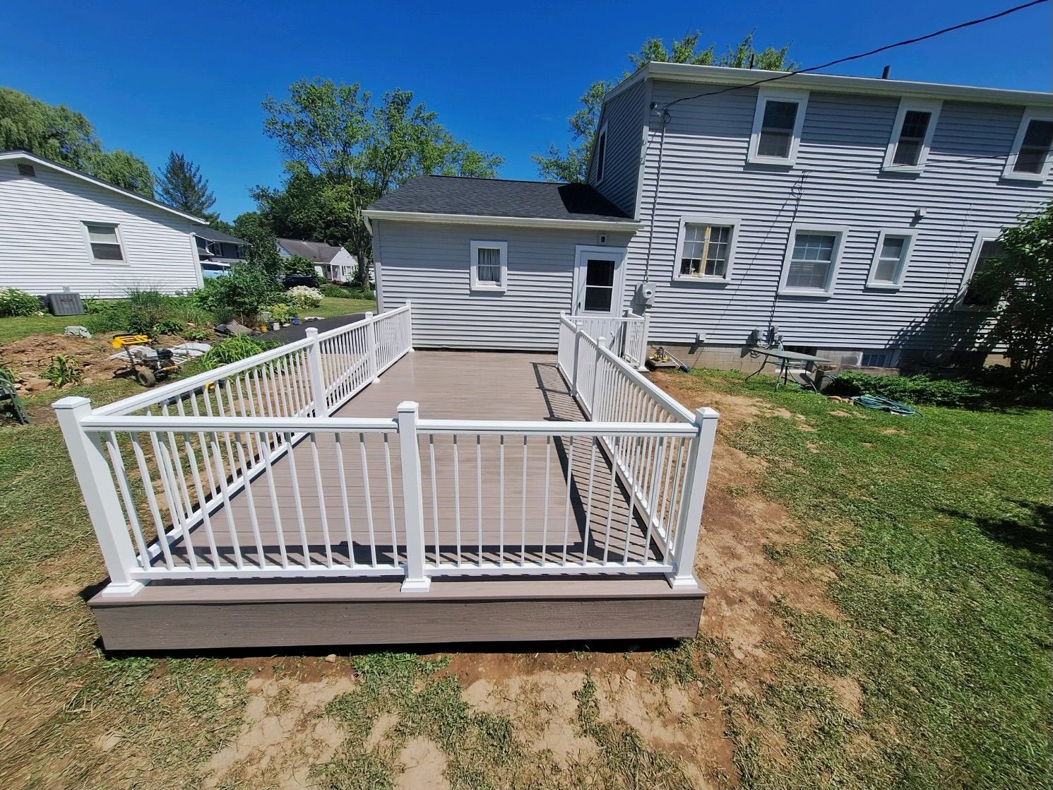A composite deck with white railing in a backyard with two-story house in the background.