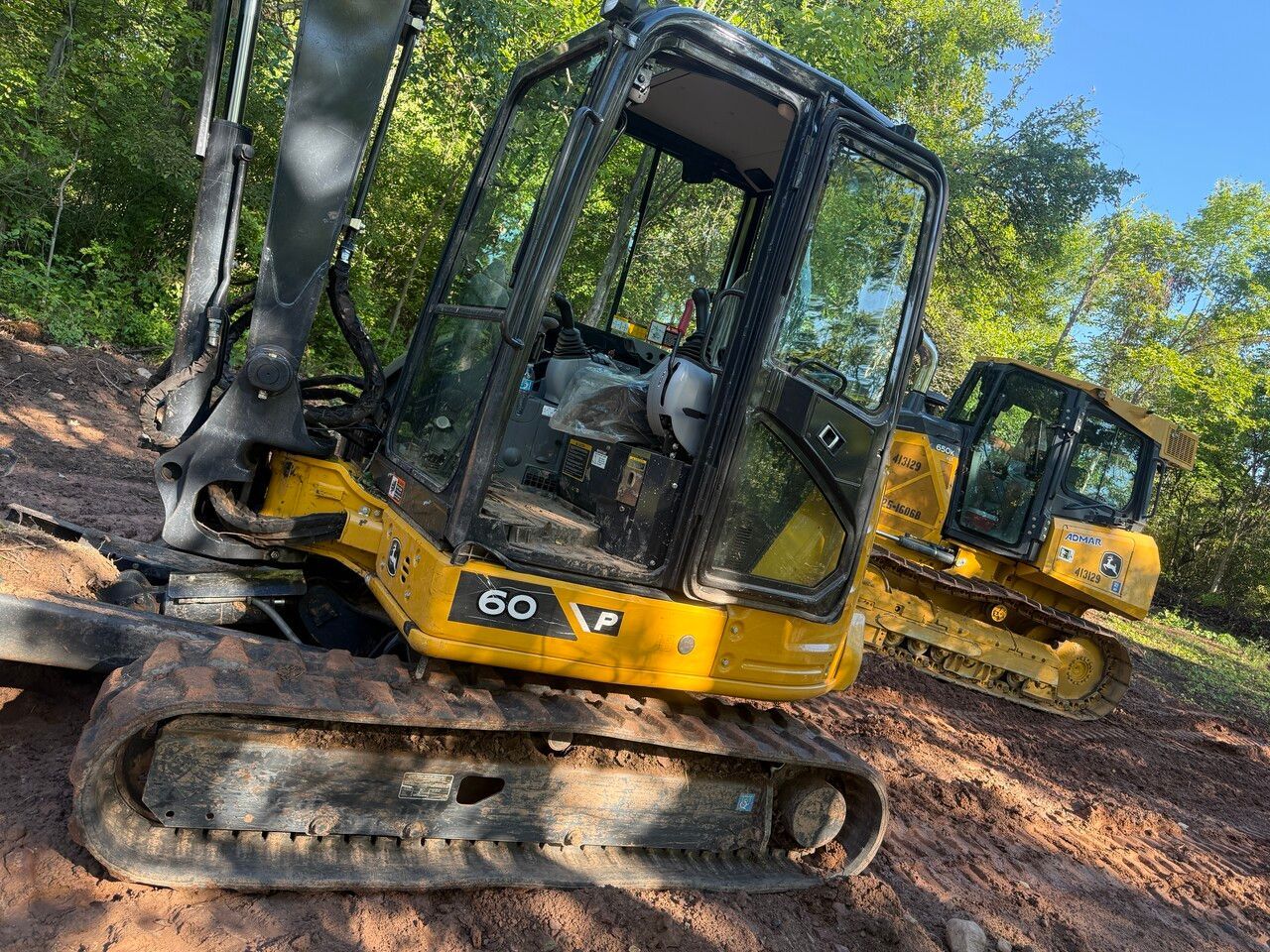 Yellow excavator machine on a dirt slope; another similar machine is in the background.