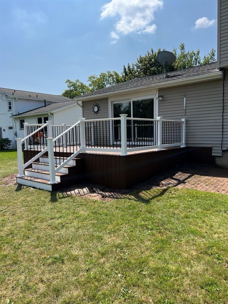 Backyard deck with white railing, black spindles, and steps. Brown deck boards.