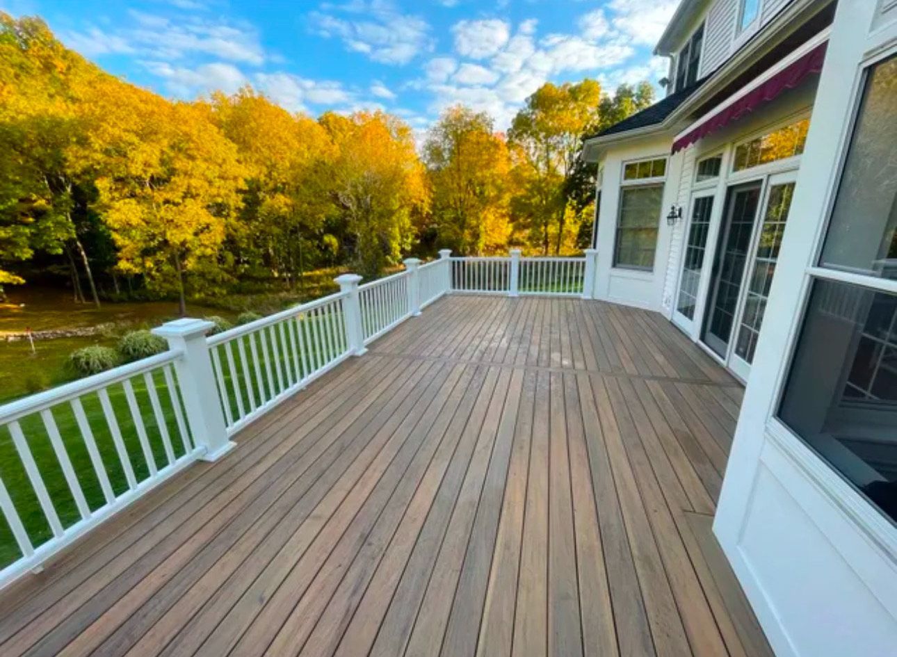 A large wooden deck with a white railing and trees in the background.
