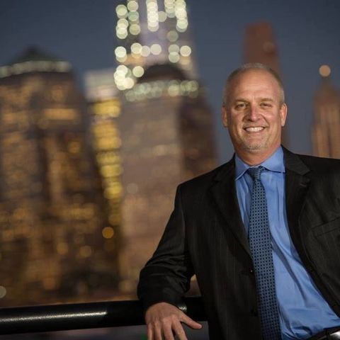 A man in a suit and tie is leaning on a railing in front of a city skyline.