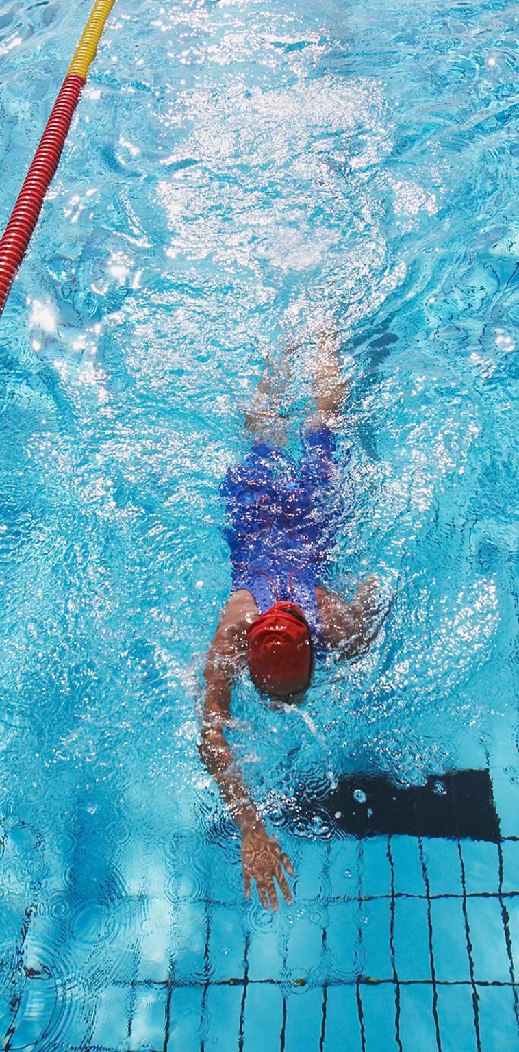 Swimmer in blue suit and red cap in pool, arm extended, overhead view.