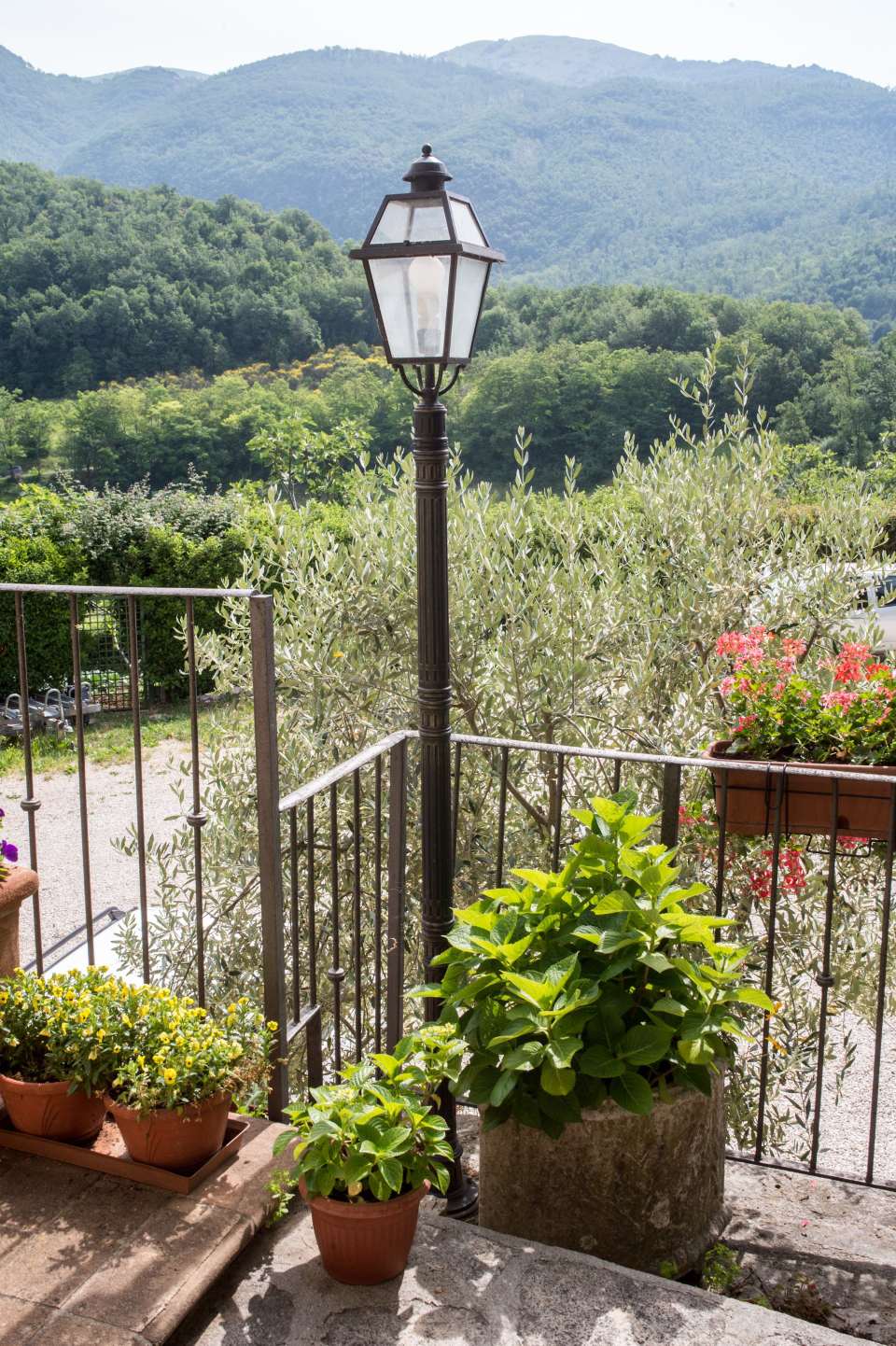 Un lampione su un balcone con piante in vaso e montagne sullo sfondo.