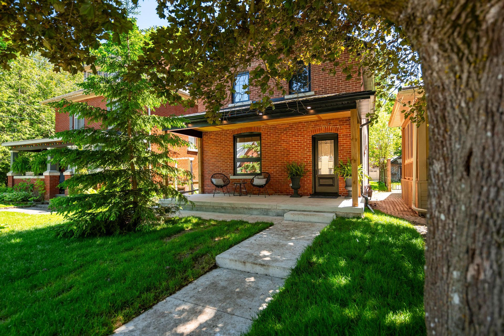 Brick house with a small porch, sidewalk, and lush green lawn under a tree.