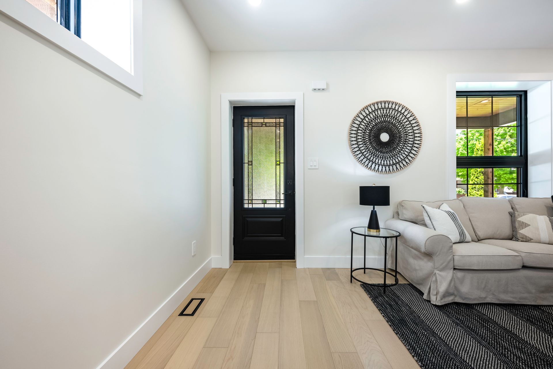 Living room with light wood floors, white walls, black door, sofa, and art.
