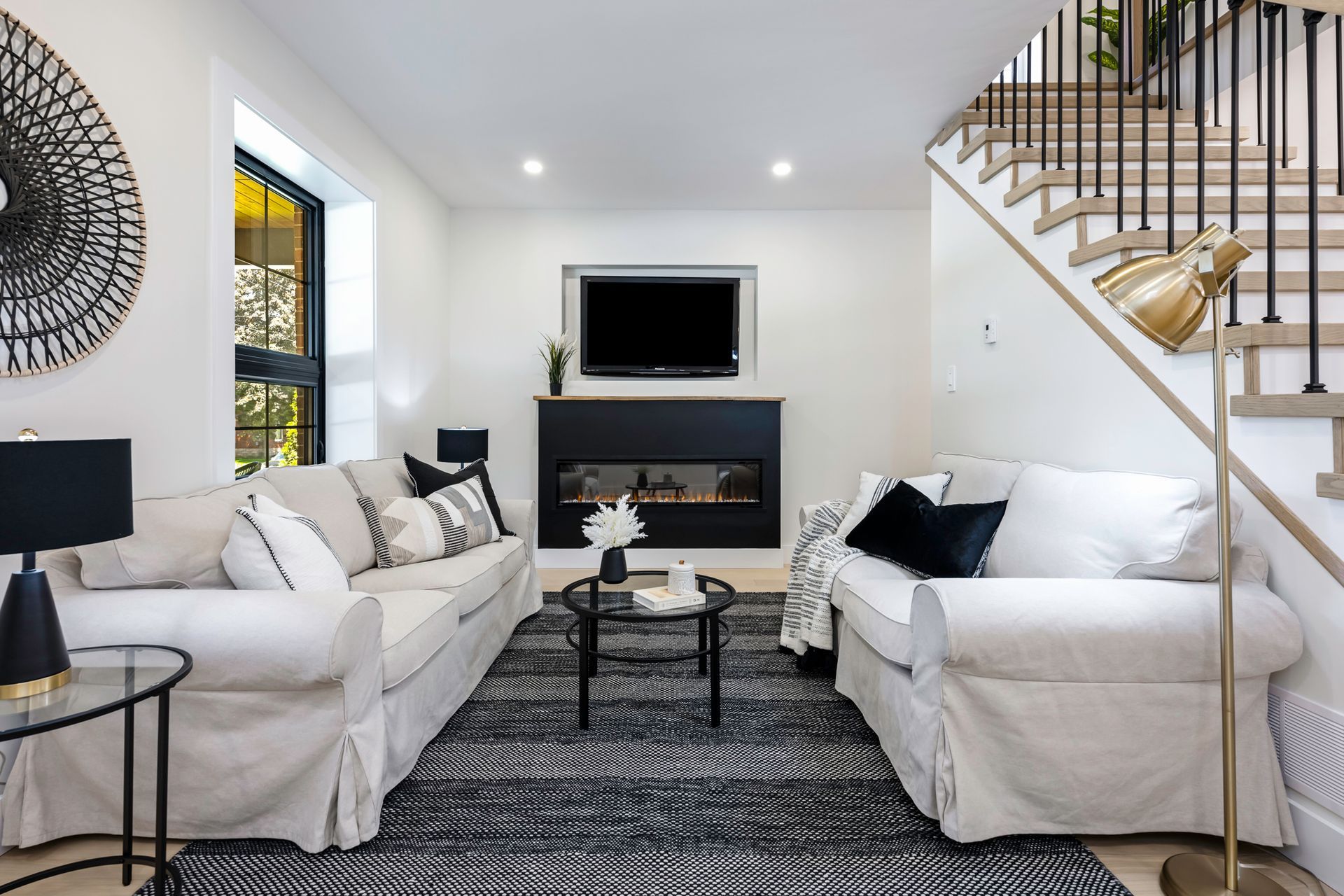 Living room with white sofas, black rug, fireplace, TV, and staircase.