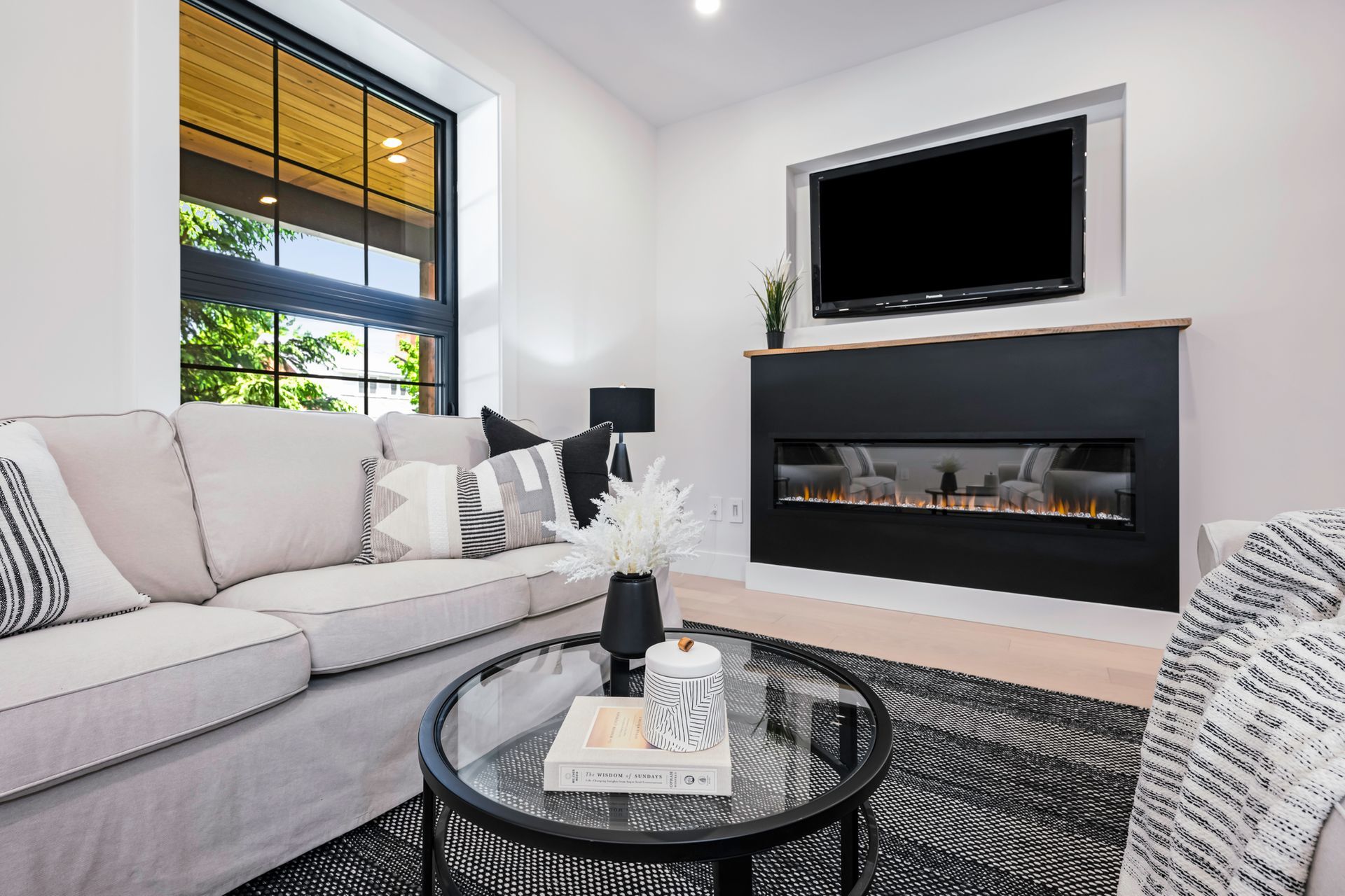 Living room with sofa, coffee table, fireplace, and TV above. Large window with a view.