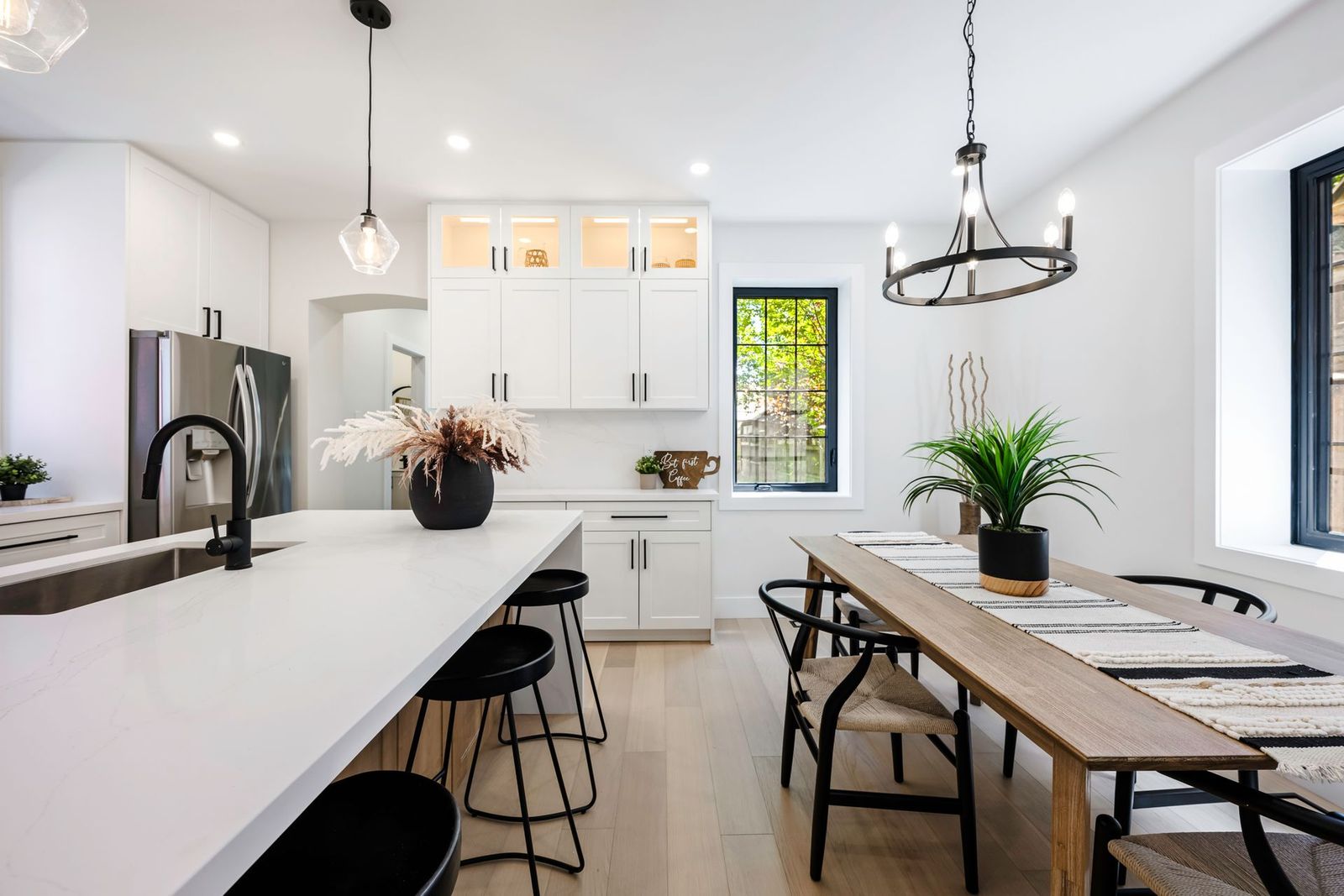 Bright modern kitchen with white cabinets, island, and dining table; black accents.