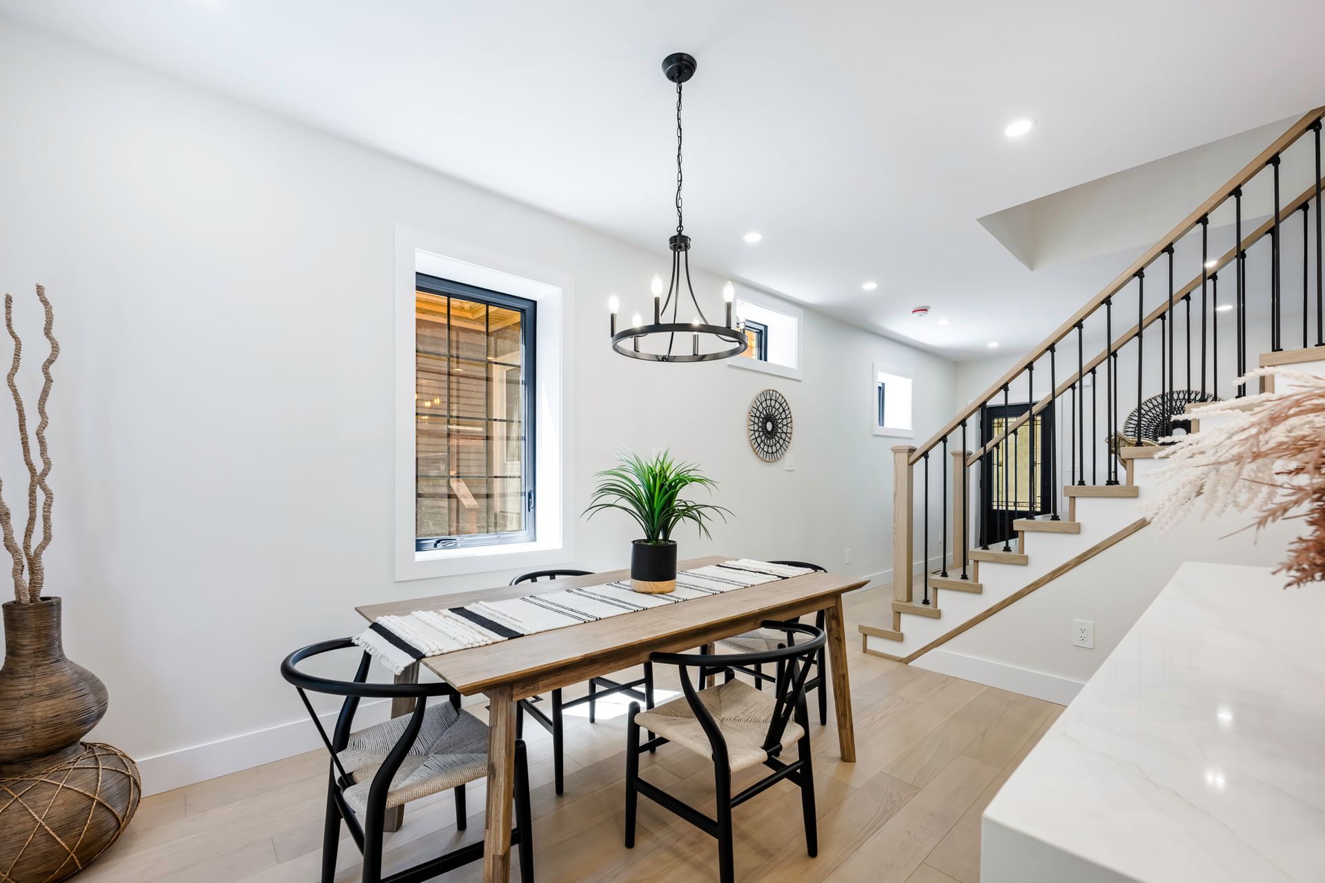 Dining room with wooden table, black chairs, chandelier, stairs, and a window.