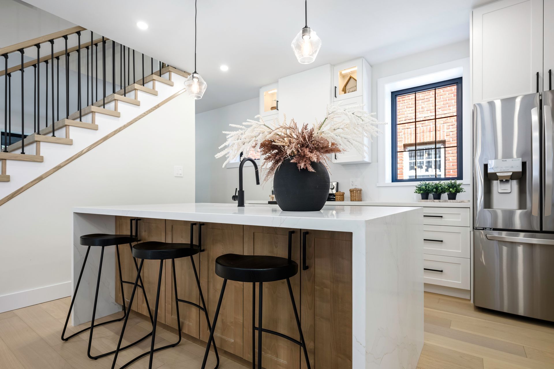 Modern kitchen with island, black stools, and stainless steel refrigerator.