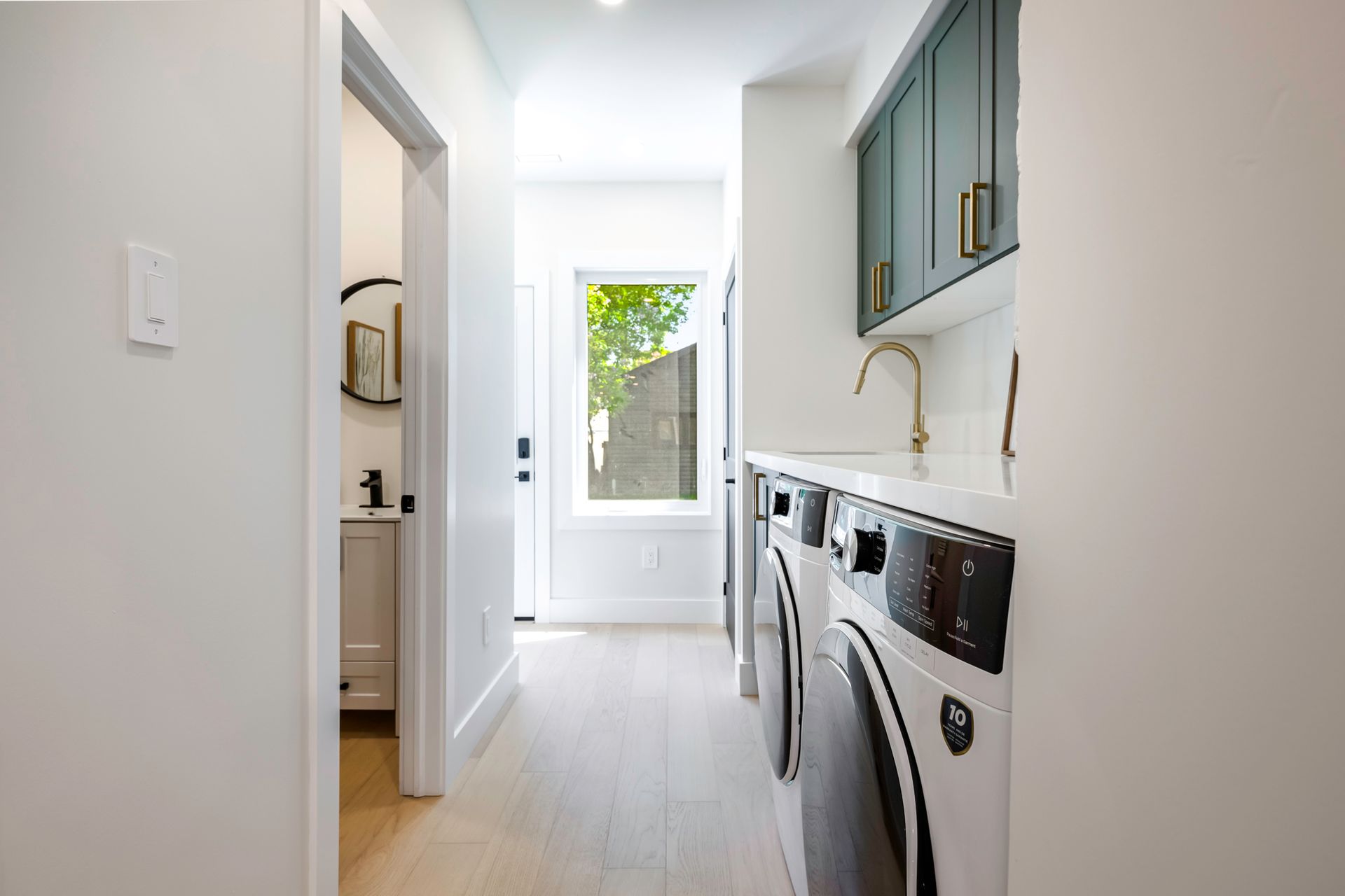 Laundry room with white appliances, teal cabinets, and a window.
