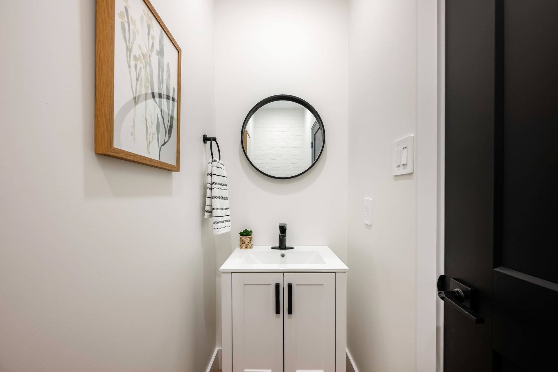 White powder room with black accents: vanity, mirror, door, and art.