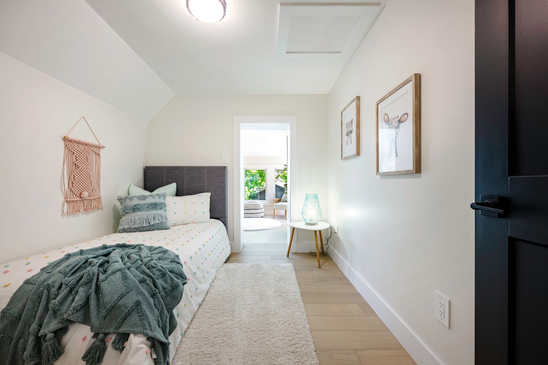 Narrow bedroom with a bed, art, and an open doorway to another room.
