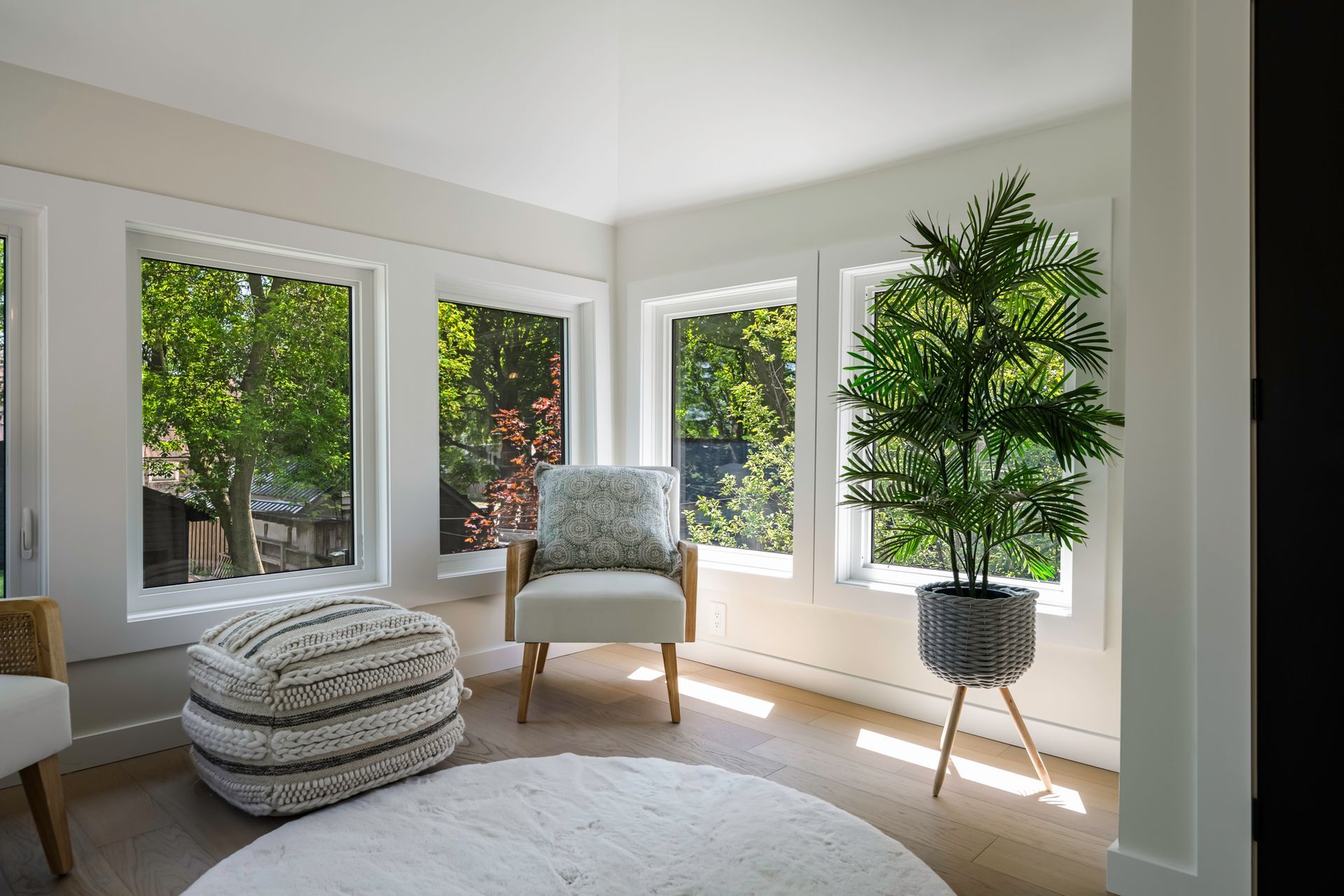 Bright sunroom with multiple windows, armchair, ottoman, and potted plant.