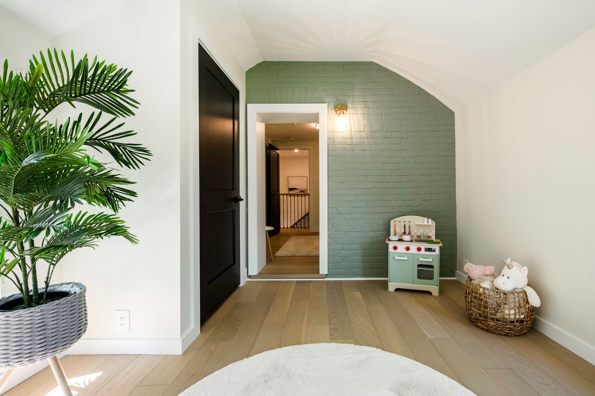 Room with green brick accent wall, black door, and a toy kitchen.