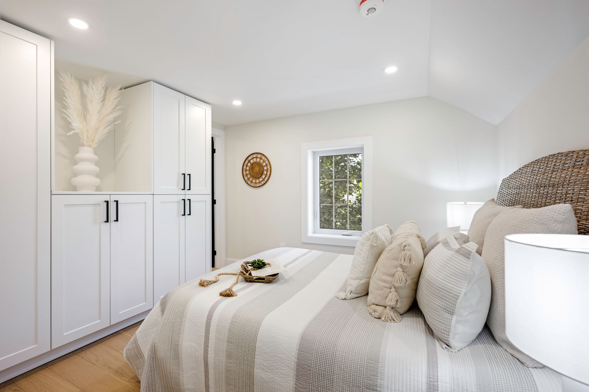 Bedroom with white cabinets, a bed with light bedding, and a window.