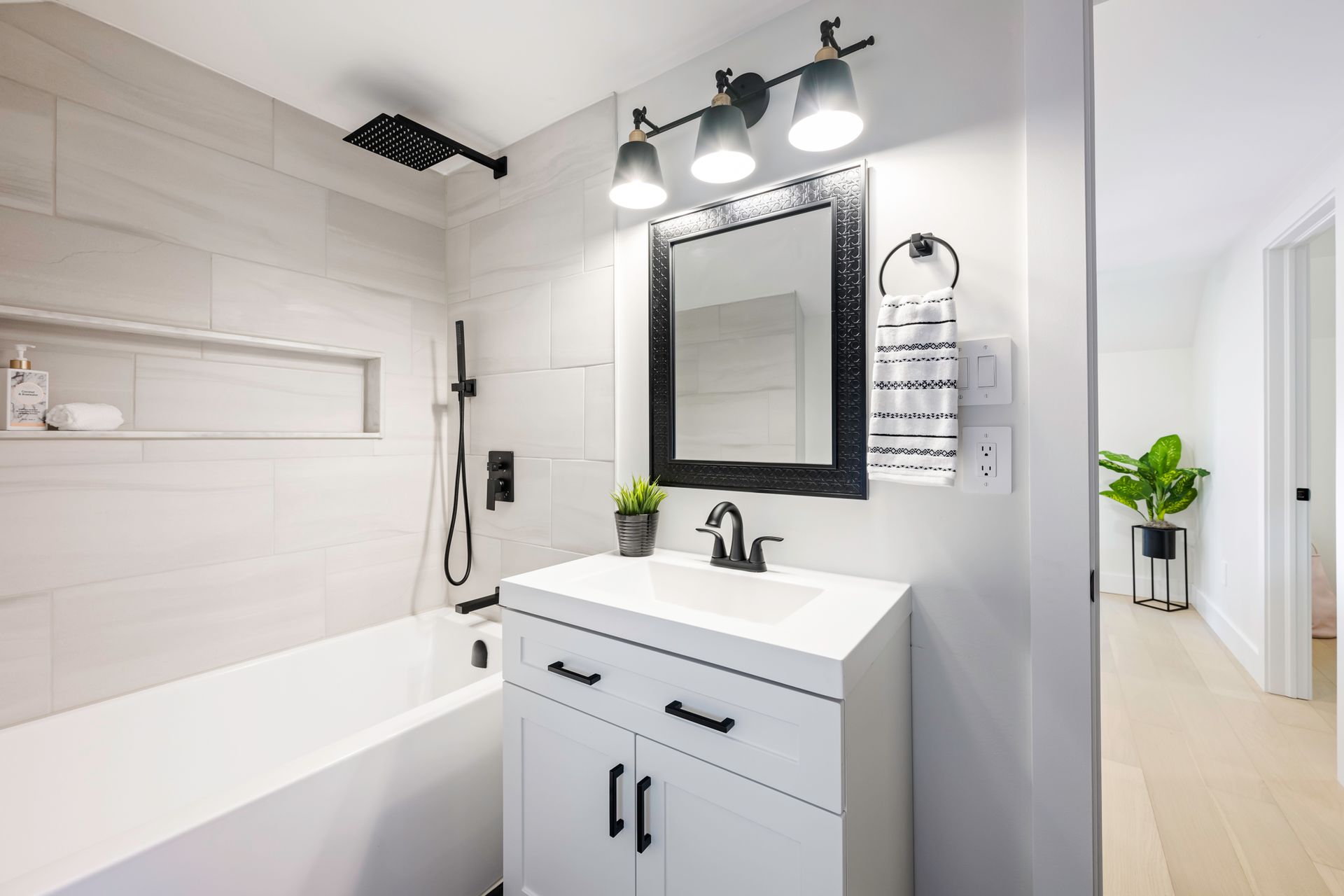 Modern white bathroom with black fixtures; includes a tub, vanity, and shower.