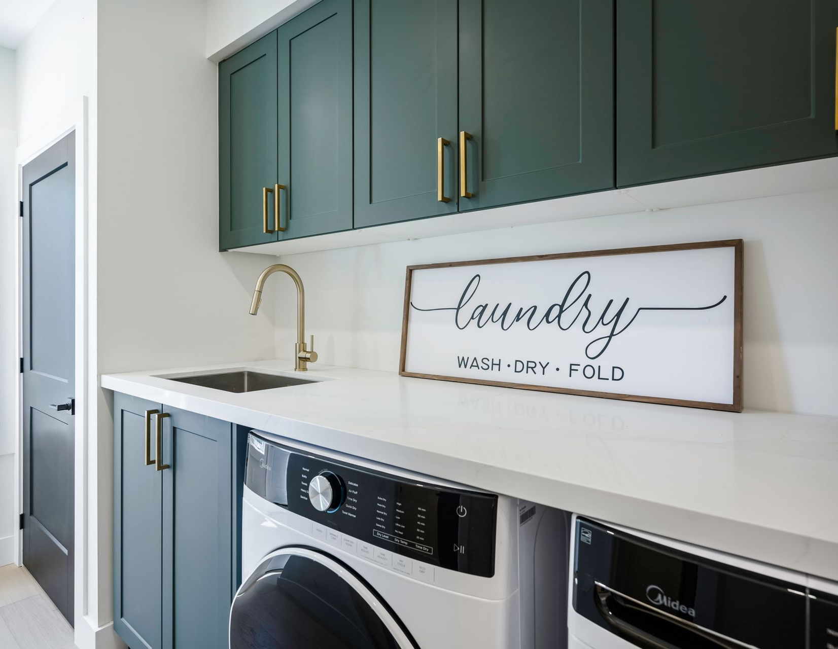 Laundry room with teal cabinets, white countertops, and washer/dryer. 