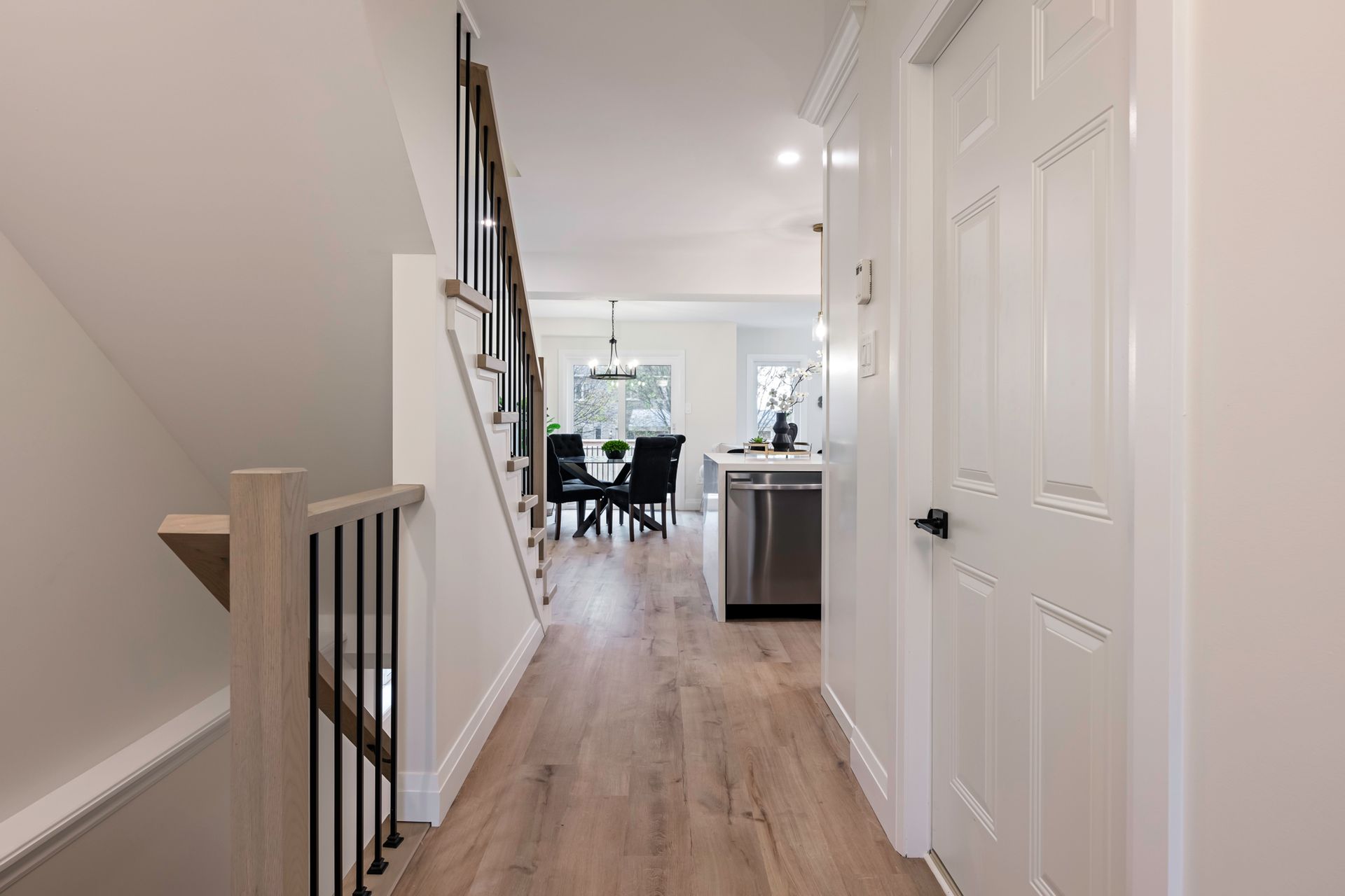 Hallway with stairs and doorway leading to dining area. Light wood flooring and white walls.
