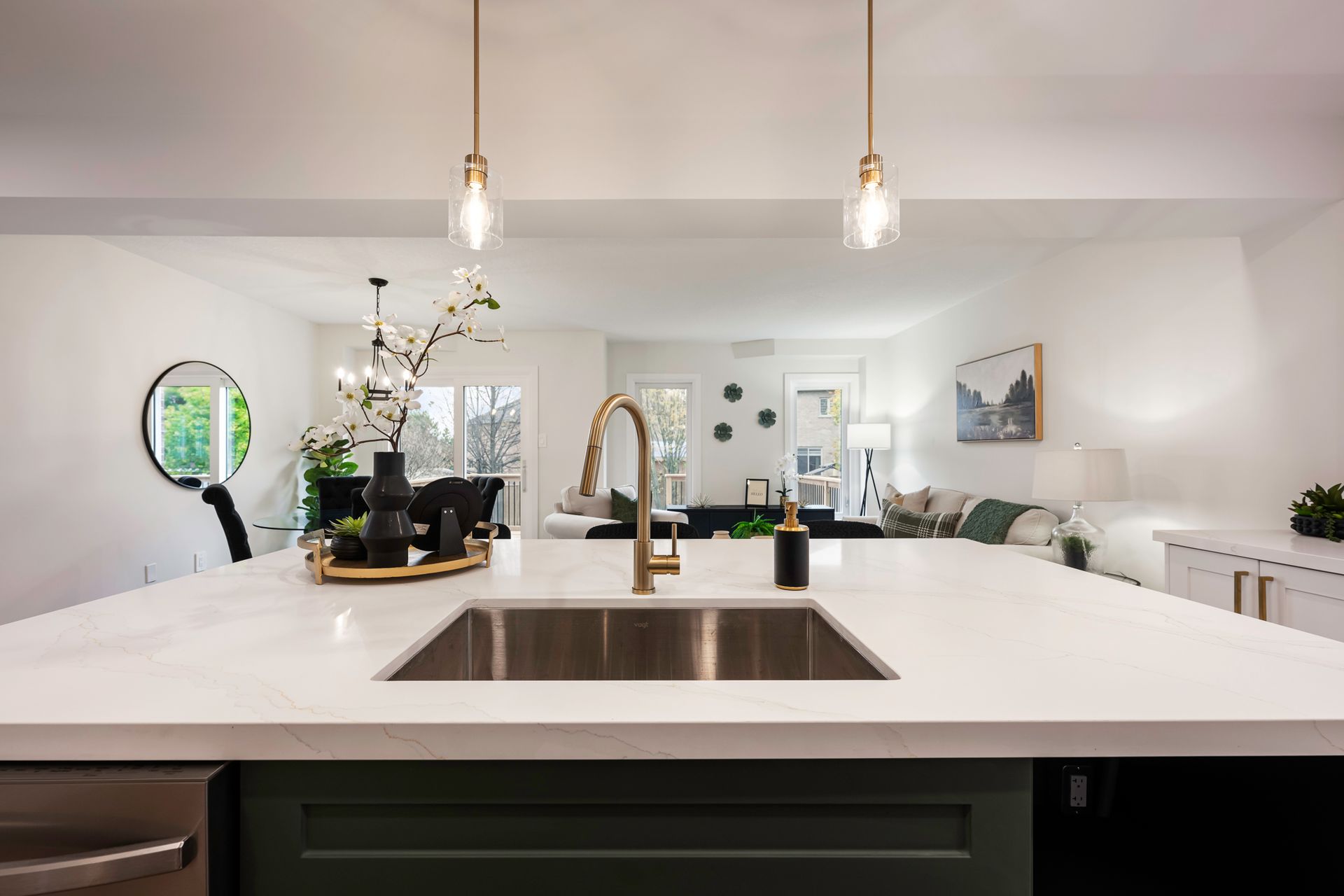 Modern kitchen with green island, white countertops, open to living area. Gold faucet, pendant lights.