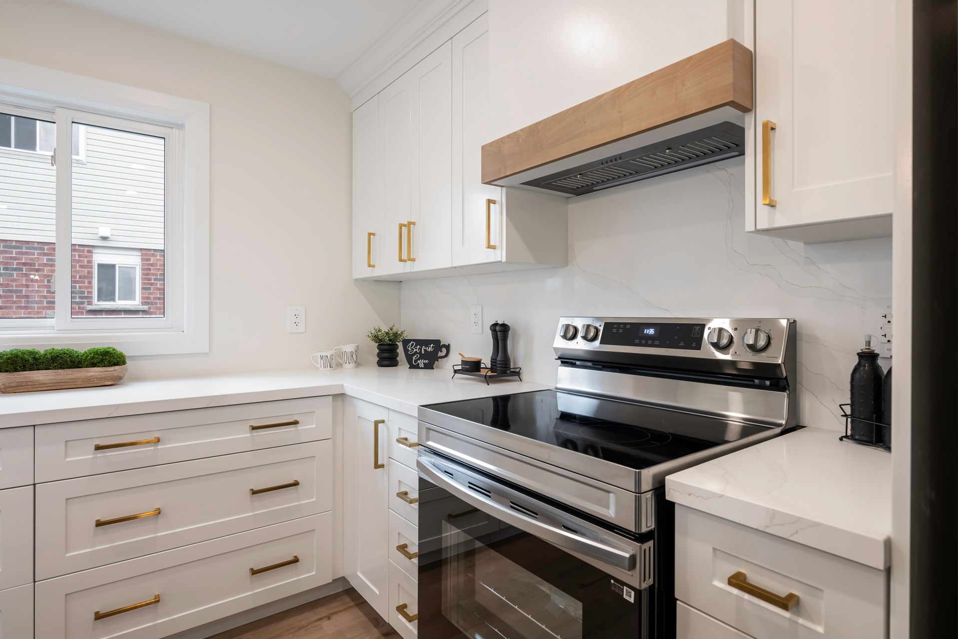 White kitchen with cabinets, stove, and range hood, with gold hardware.