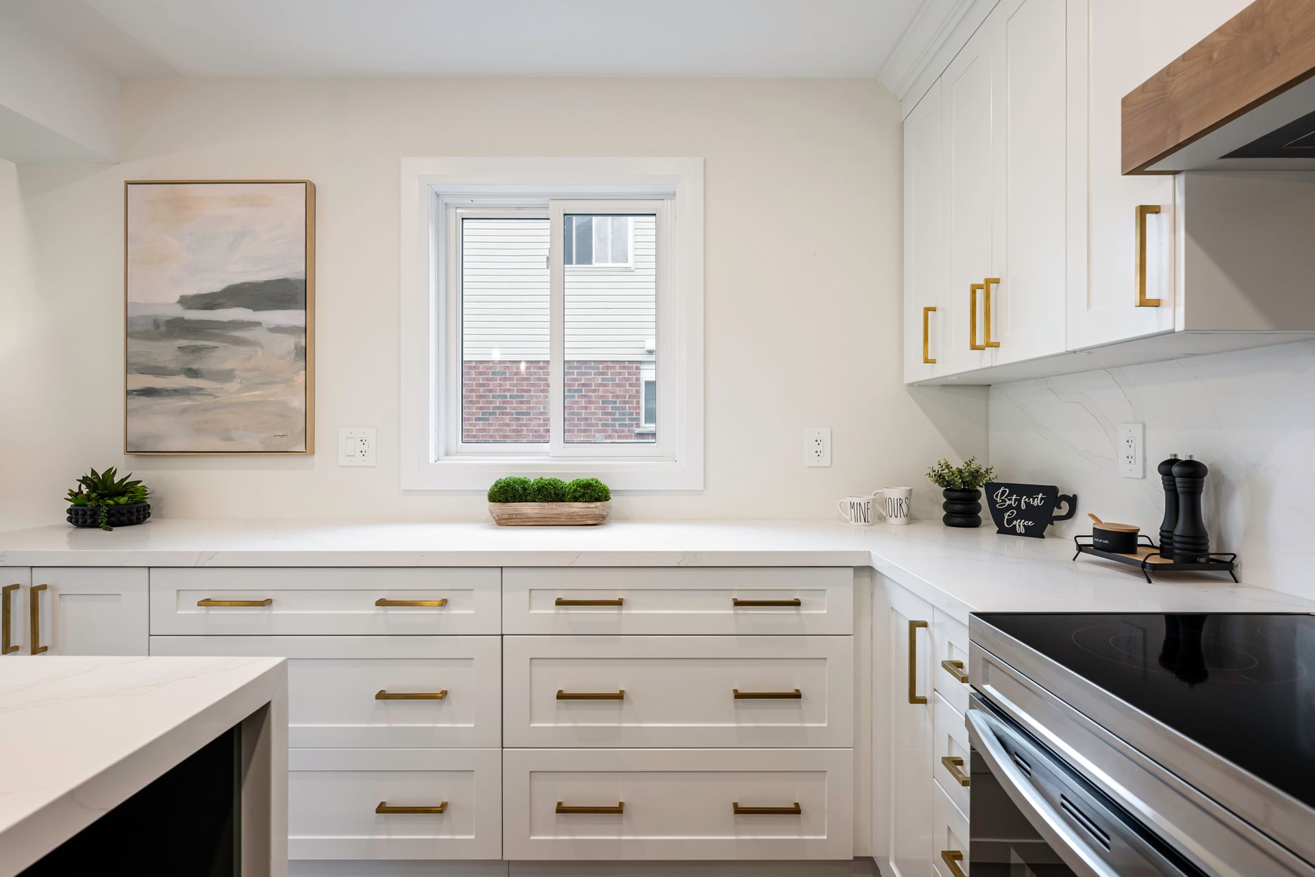 White kitchen with gold hardware, marble countertops, and an island. A window is above the countertop.
