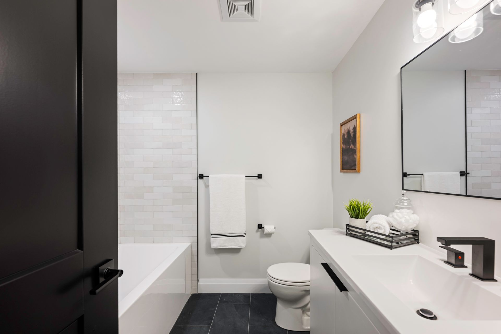 Modern bathroom with white walls, black accents, tub, toilet, and vanity.
