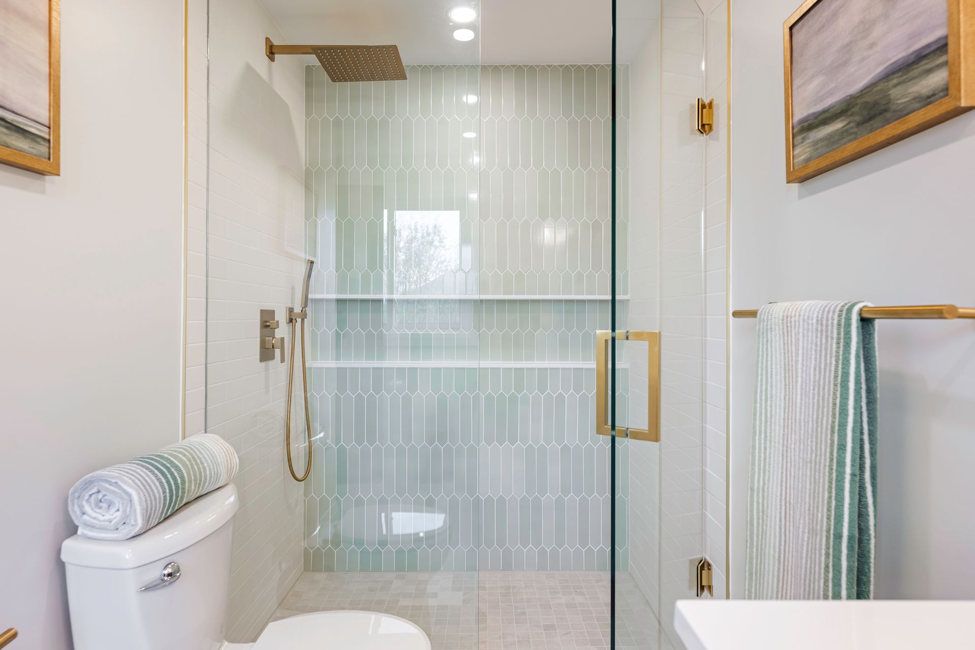 Modern bathroom with glass shower, light green tile, gold fixtures, and white walls.