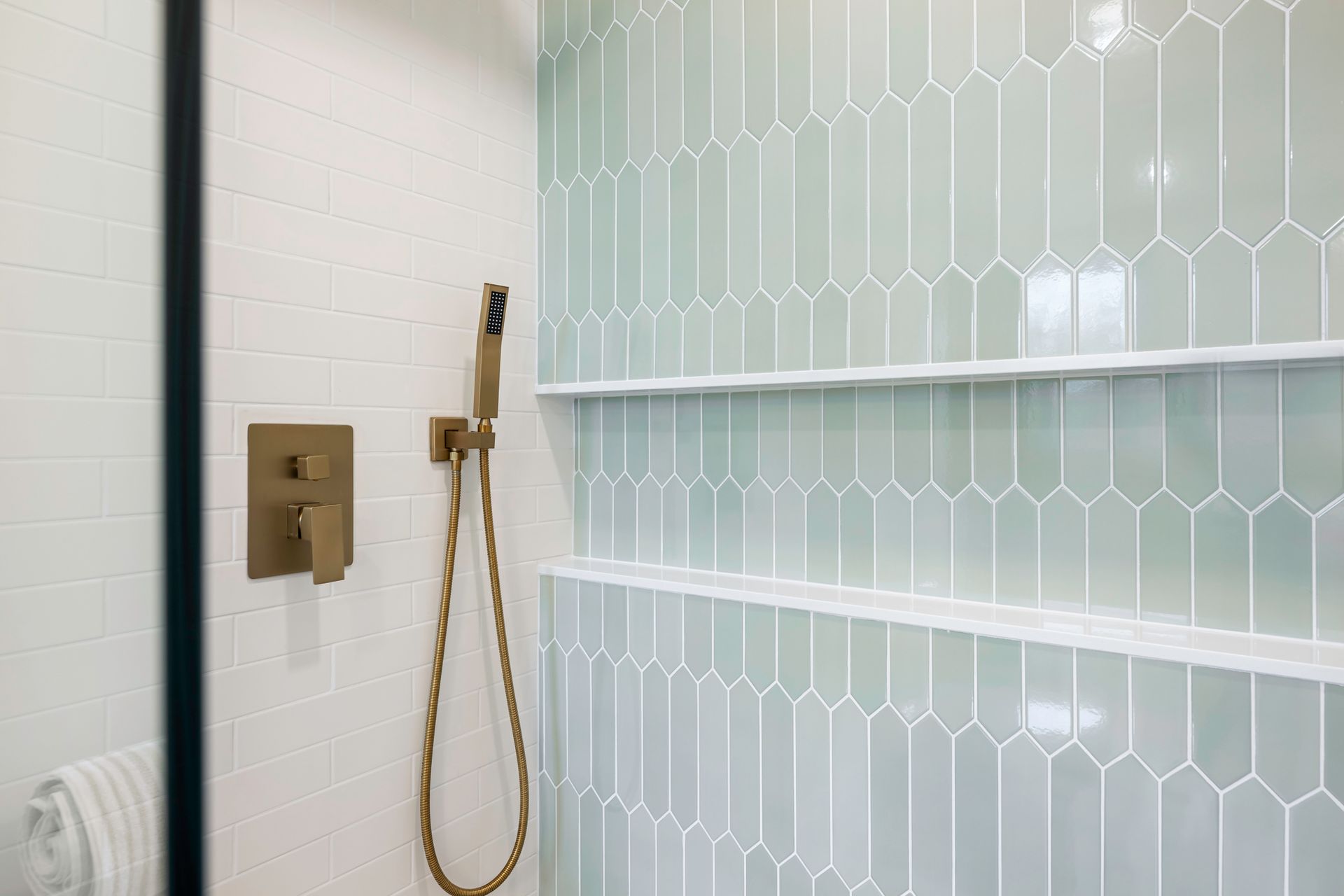Shower interior with pale green geometric tile, built-in shelves, and brass fixtures.